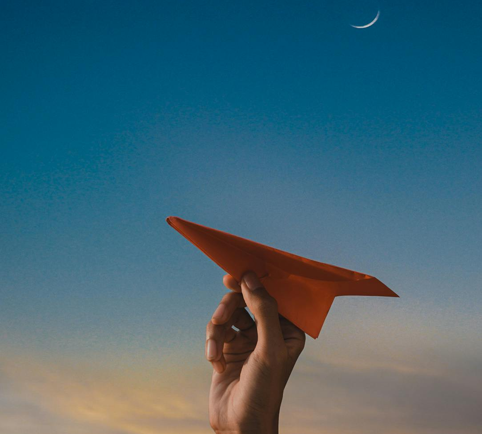 Hand holding paper airplane against twilight sky